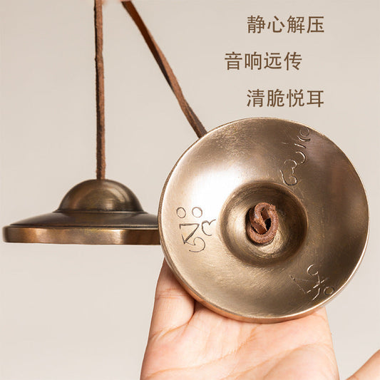 Bronzetide – Hand holding one bronze Ding Xia bell showing engraved symbols and knotted leather cord inside the cup