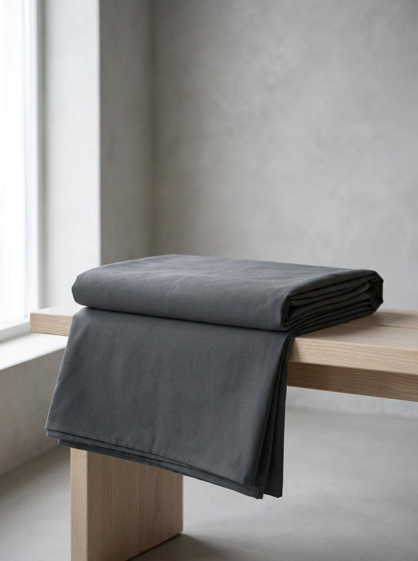 A folded charcoal cotton meditation blanket resting on a pale wooden bench.